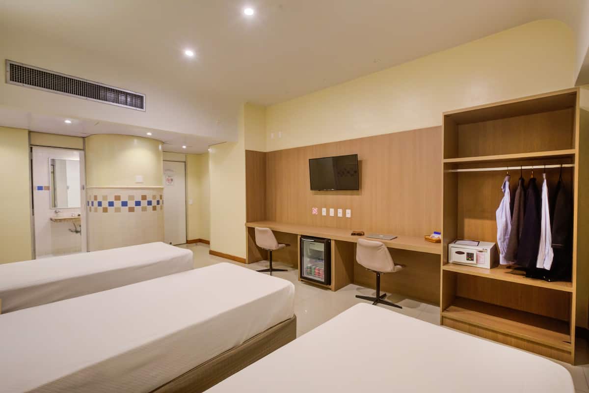 Une chambre d’hôtel avec deux lits, un bureau avec un ordinateur, une télévision, un mini-réfrigérateur et une armoire.