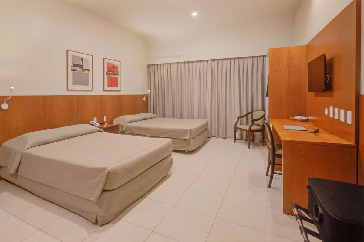 Une chambre d’hôtel avec deux lits, un bureau, une chaise et une télévision.
