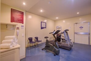 Un gimnasio con equipo de ejercicio, toallas y un cartel con normas.