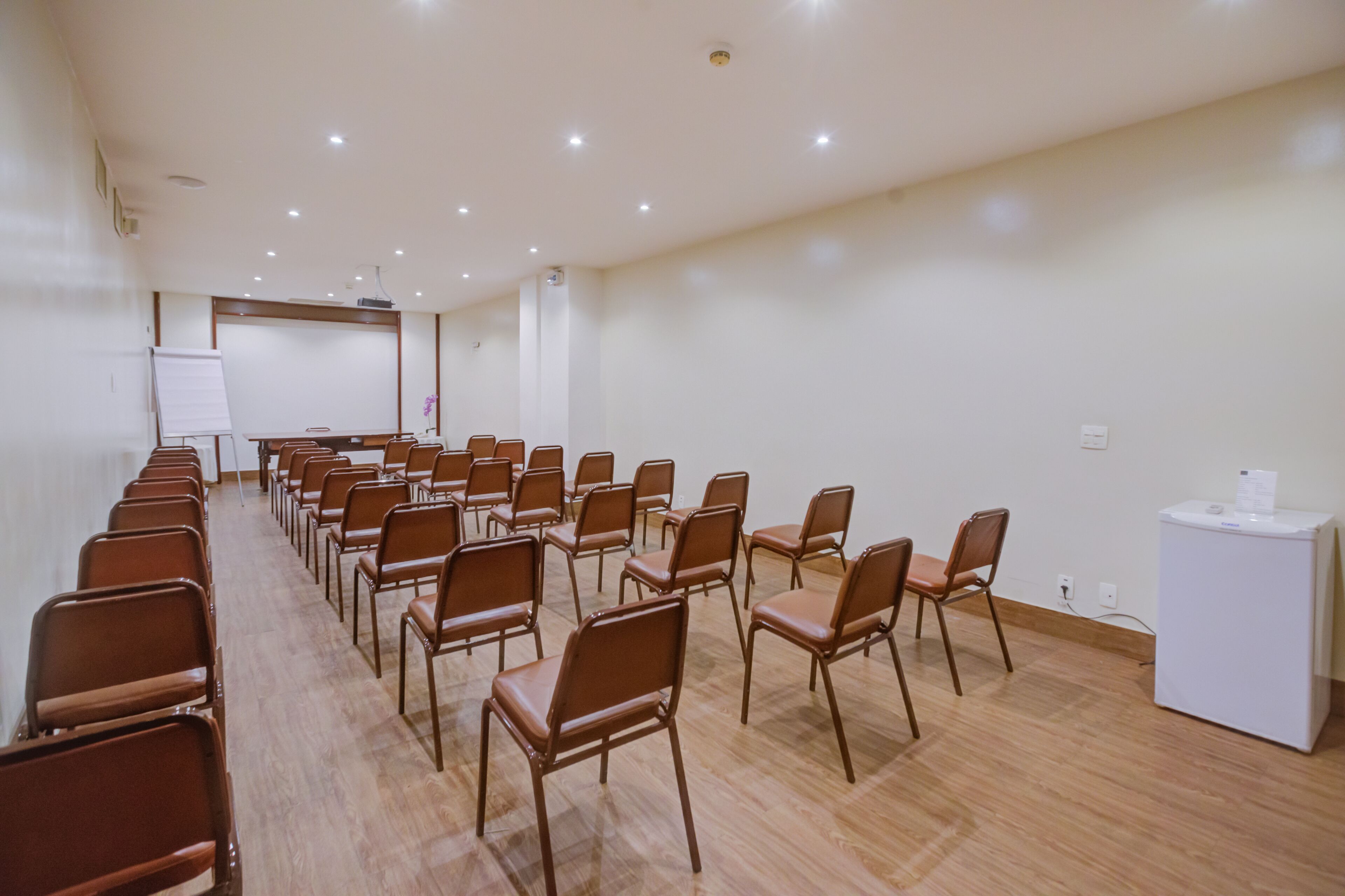 A conference room with rows of brown chairs, a whiteboard, and a white podium.