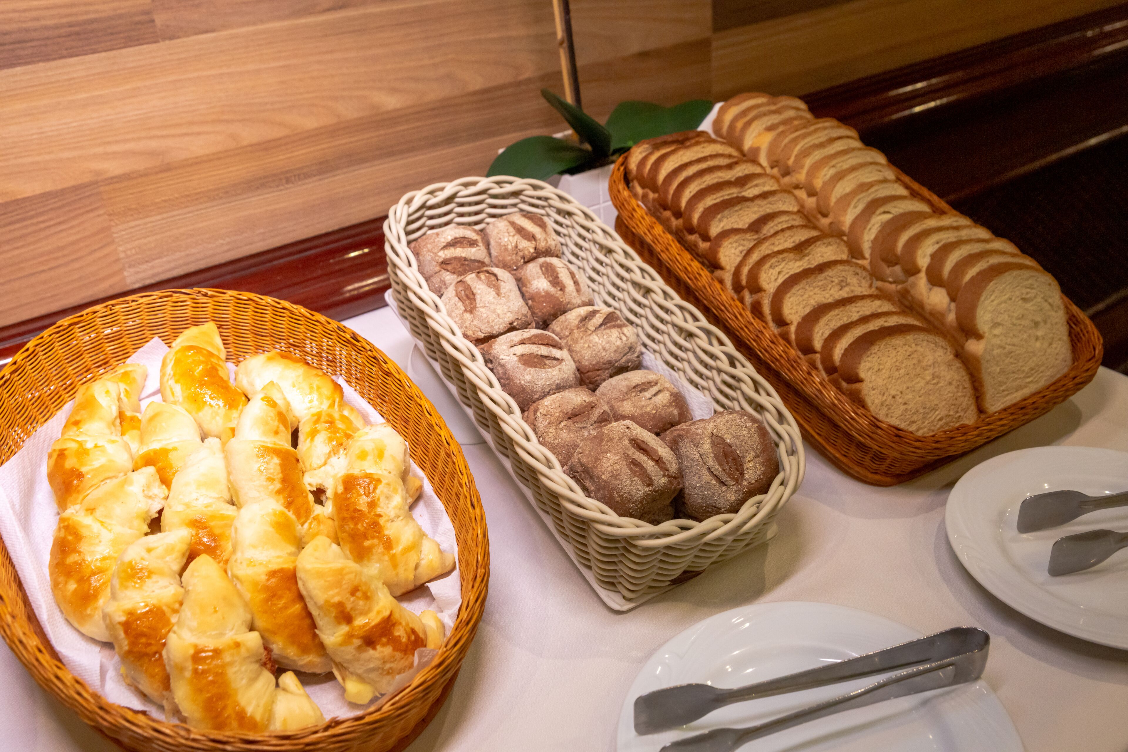 A table with various bread and pastries in baskets and on plates, with a wooden background.