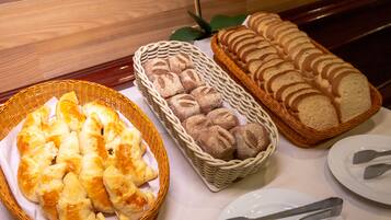 A table with various bread and pastries in baskets and on plates, with a wooden background.
