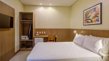 Una habitación de hotel con cama, escritorio, silla, televisor y un cuadro en la pared.