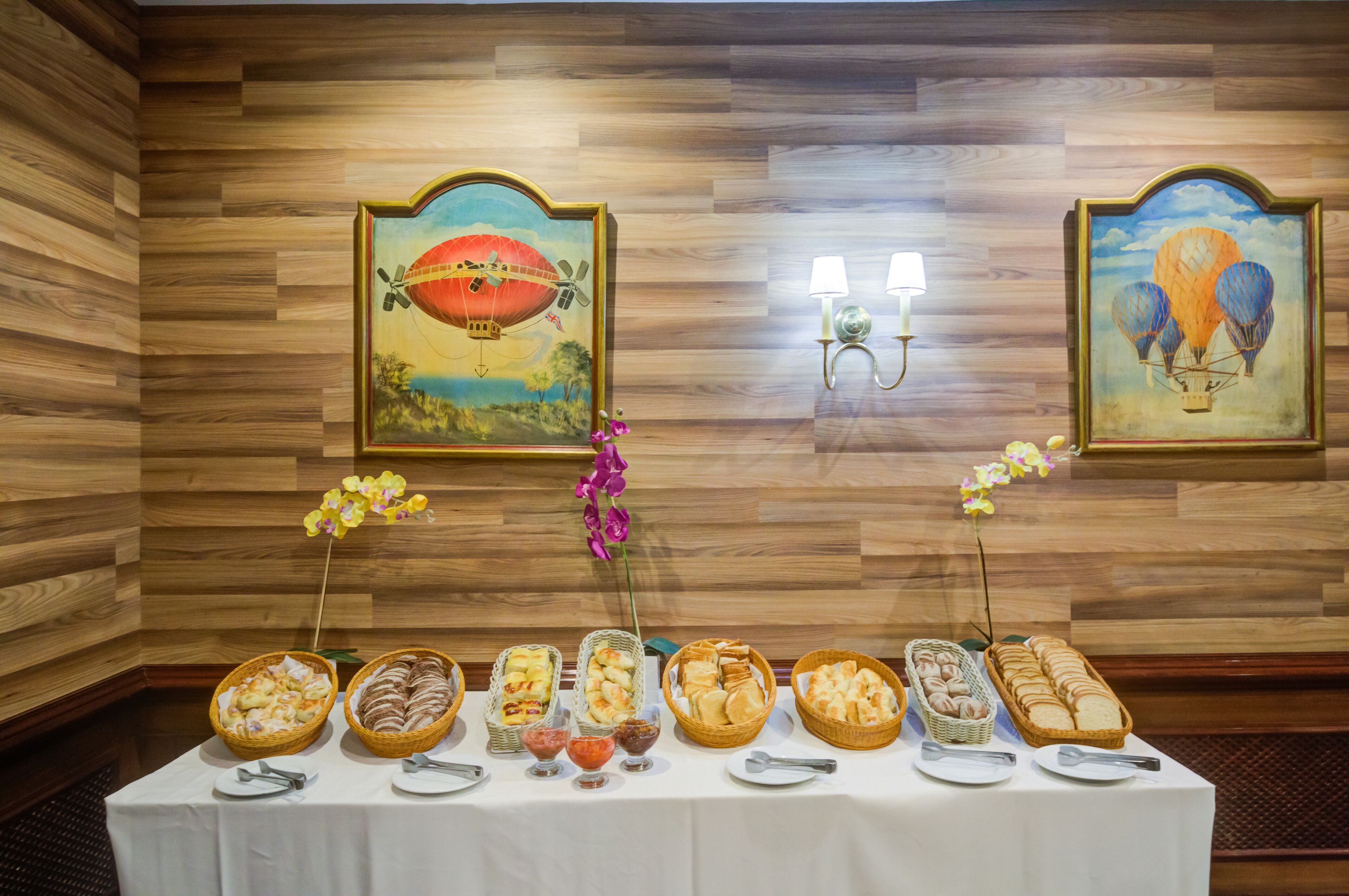 A buffet table with various food items and decorative flowers, set against a wooden wall with framed paintings.