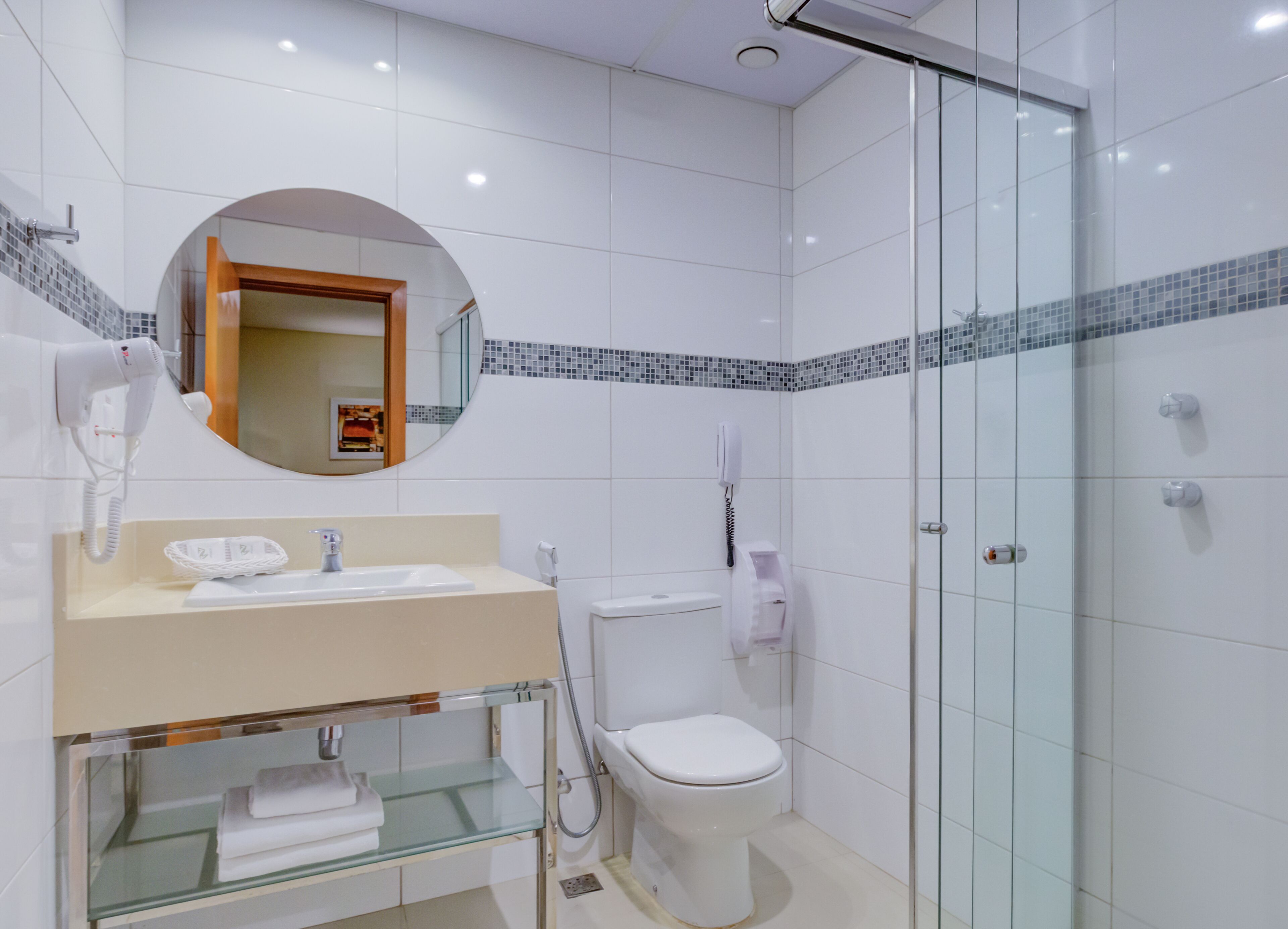 Un bagno moderno con cabina doccia in vetro, un water, un lavandino con specchio e un asciugacapelli.