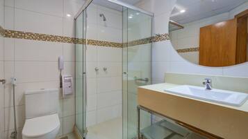 Une salle de bain avec une douche à parois de verre, des toilettes blanches, un lavabo avec un miroir et un sol carrelé.