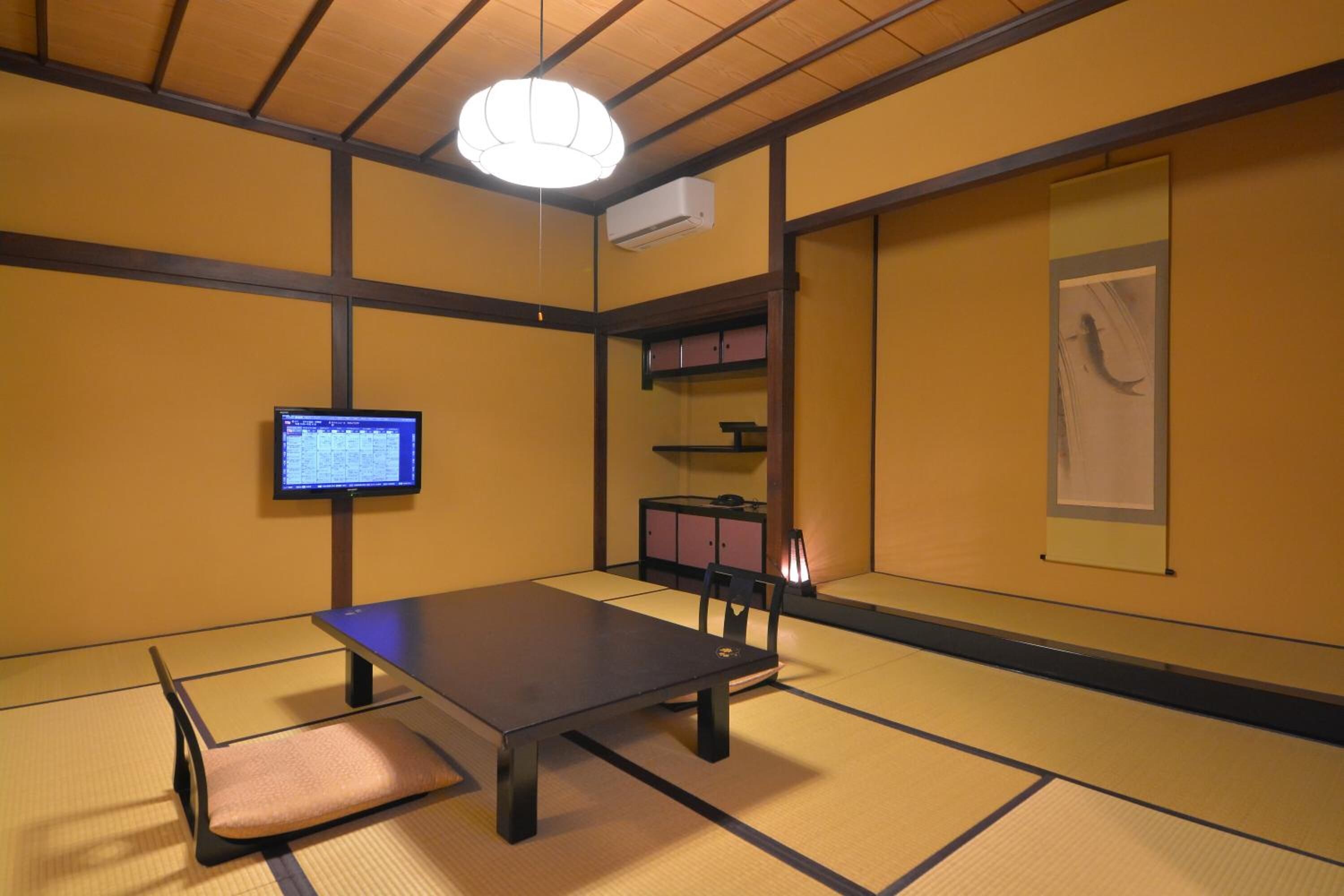 A traditional tatami mat room with a low table, a chair, a television, and a cabinet.