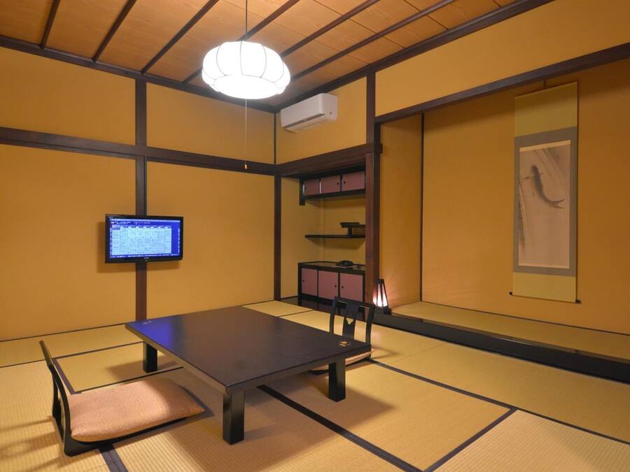 A traditional tatami mat room with a low table, a chair, a television, and a cabinet.