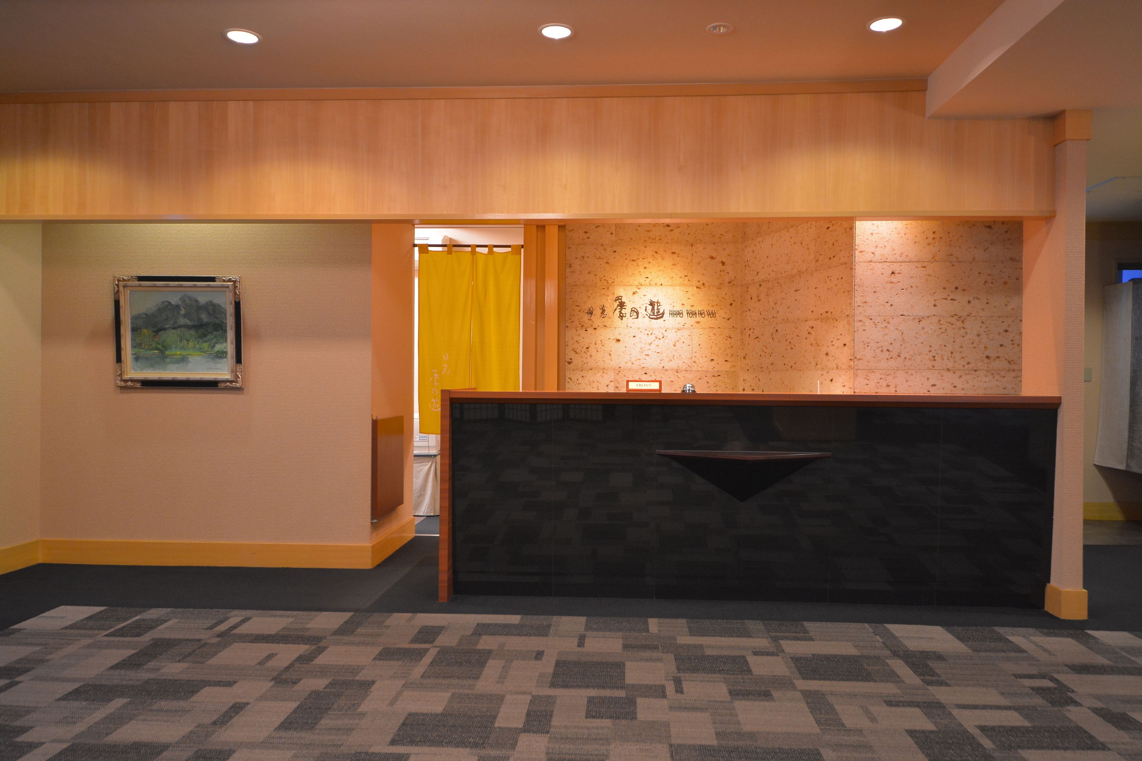 A reception area with a wooden reception desk, a framed painting on the wall, and a patterned carpet.