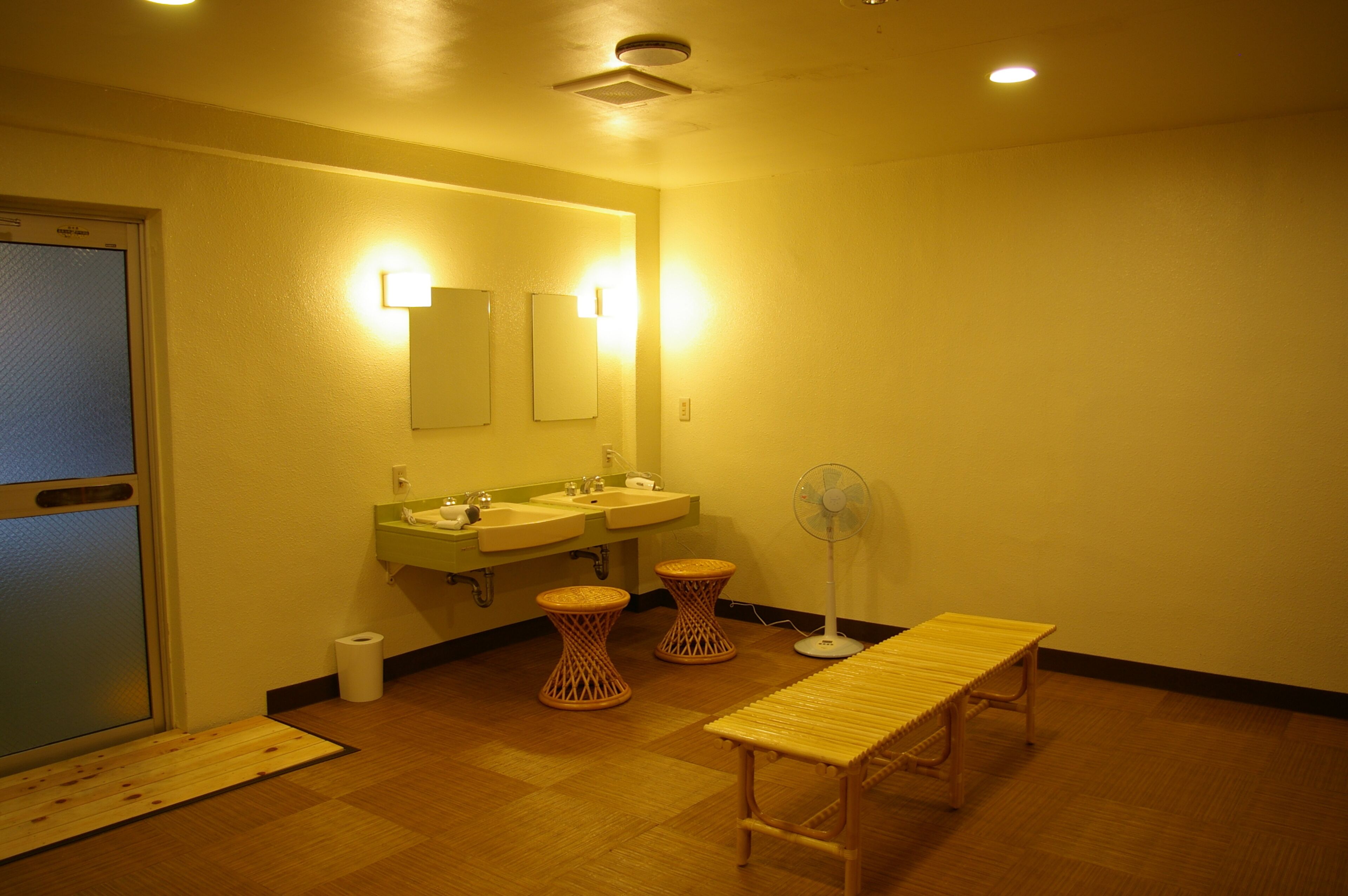 Ein Badezimmer mit zwei Waschbecken, einem Spiegel, einem Ventilator und einer Sitzbank.