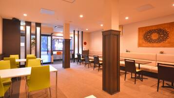 A modern restaurant with yellow chairs, white tables, and a large decorative wall piece.