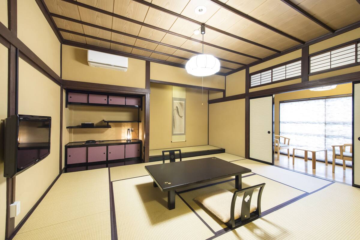 A tatami room with a tatami mat floor, a low table, and a TV on the wall.