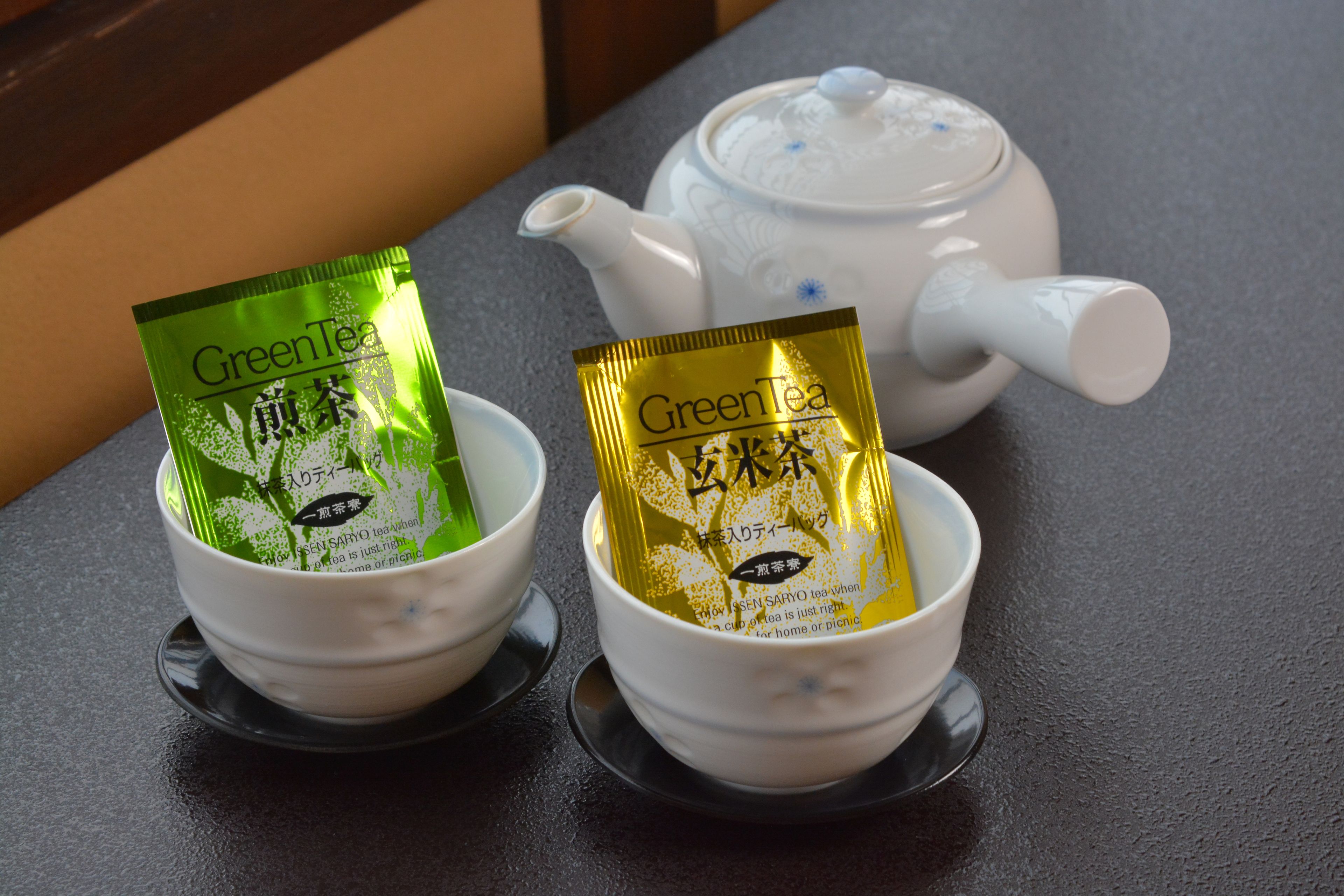 Two white teacups with green and gold tea packets on a dark surface.