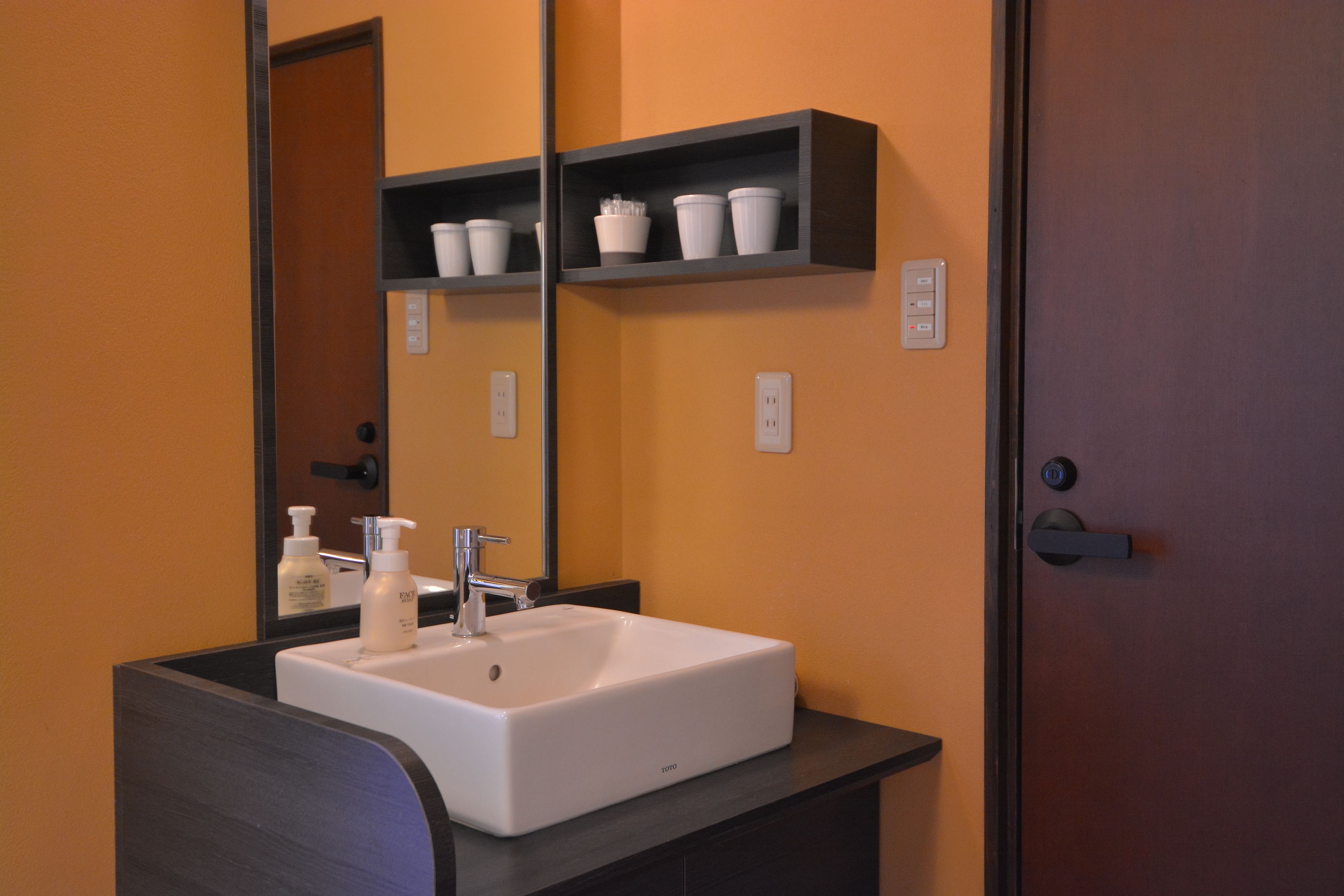 Une salle de bain avec un lavabo blanc, un miroir et une étagère contenant des articles de toilette.