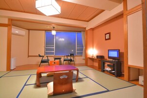 A traditional Japanese room with tatami flooring, a low table, chairs, a television, and a window with a view.