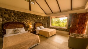 Un dormitorio con dos camas, paredes de piedra, un ventanal grande y una puerta de madera.