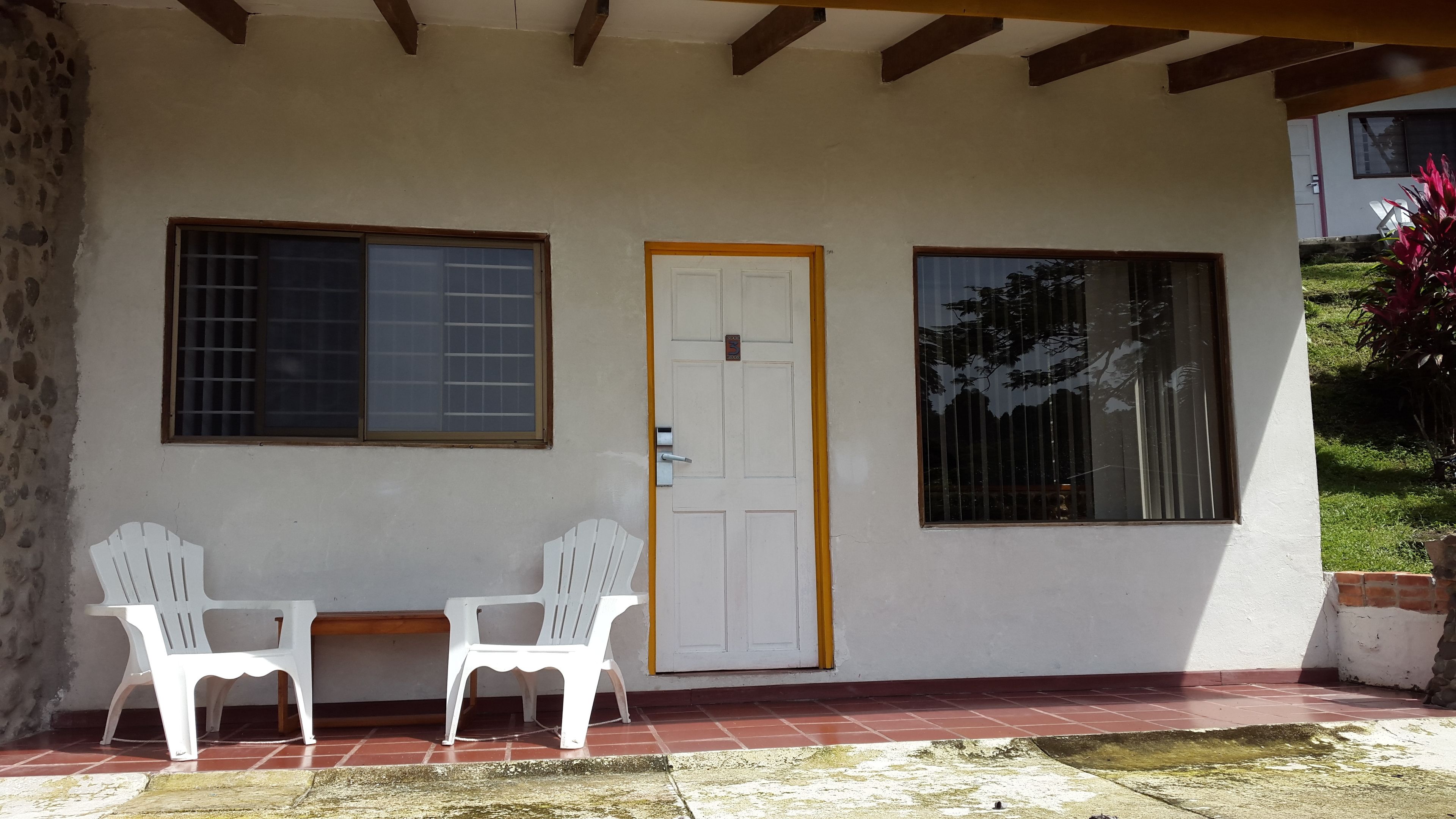 A building with a white exterior, a wooden door, and two windows with metal bars.
