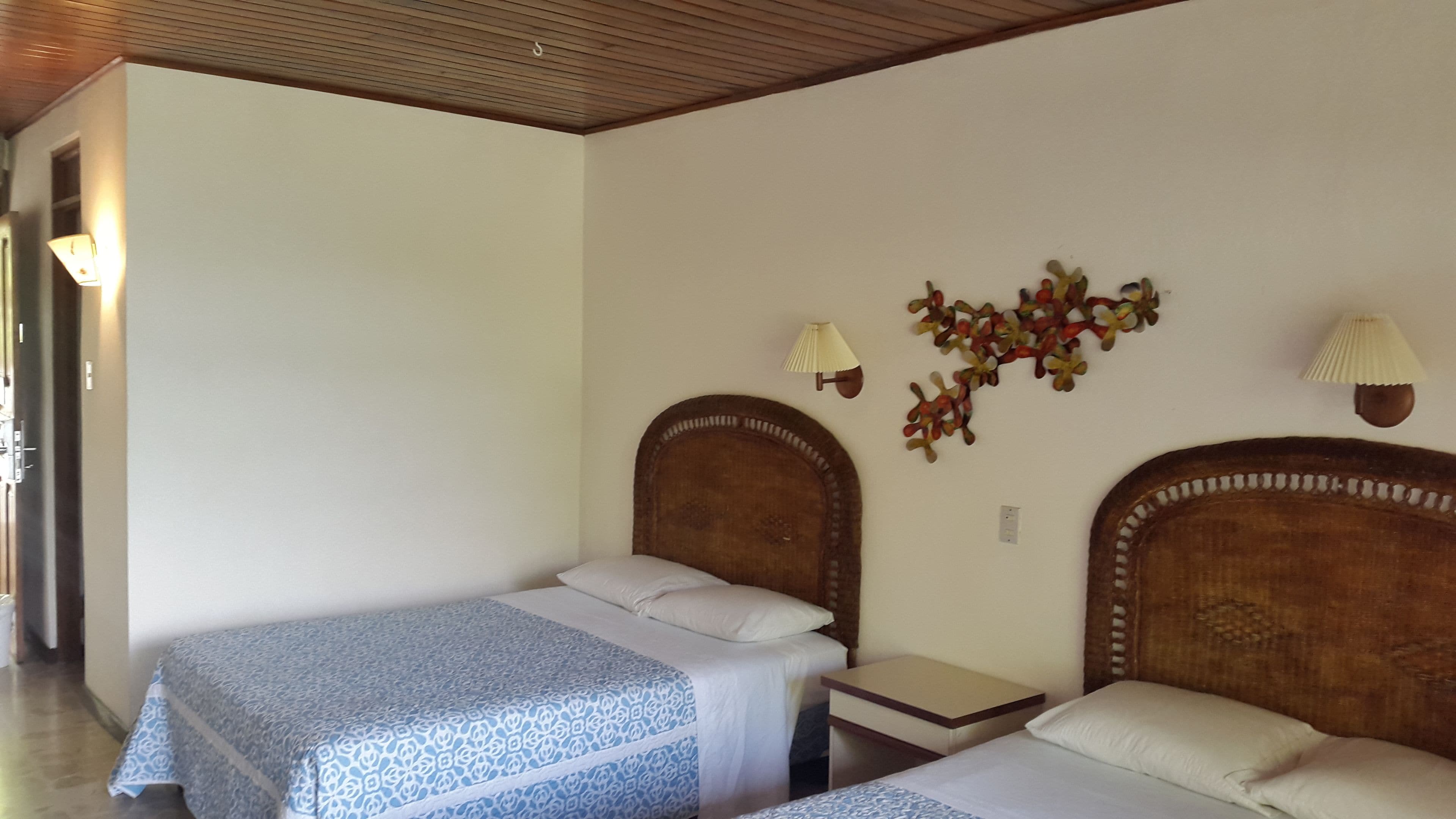 Habitación de hotel con dos camas individuales, una mesita de noche pequeña, una lámpara de pared y un adorno en la pared.