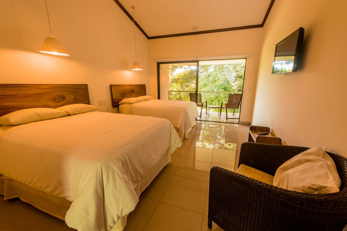 Una habitación de hotel con dos camas, un balcón con sillas y un televisor en la pared.