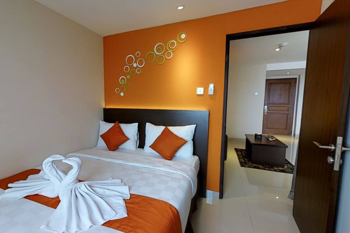 Quarto de hotel com uma cama, uma obra de arte na parede e uma porta que dá para outro cômodo.