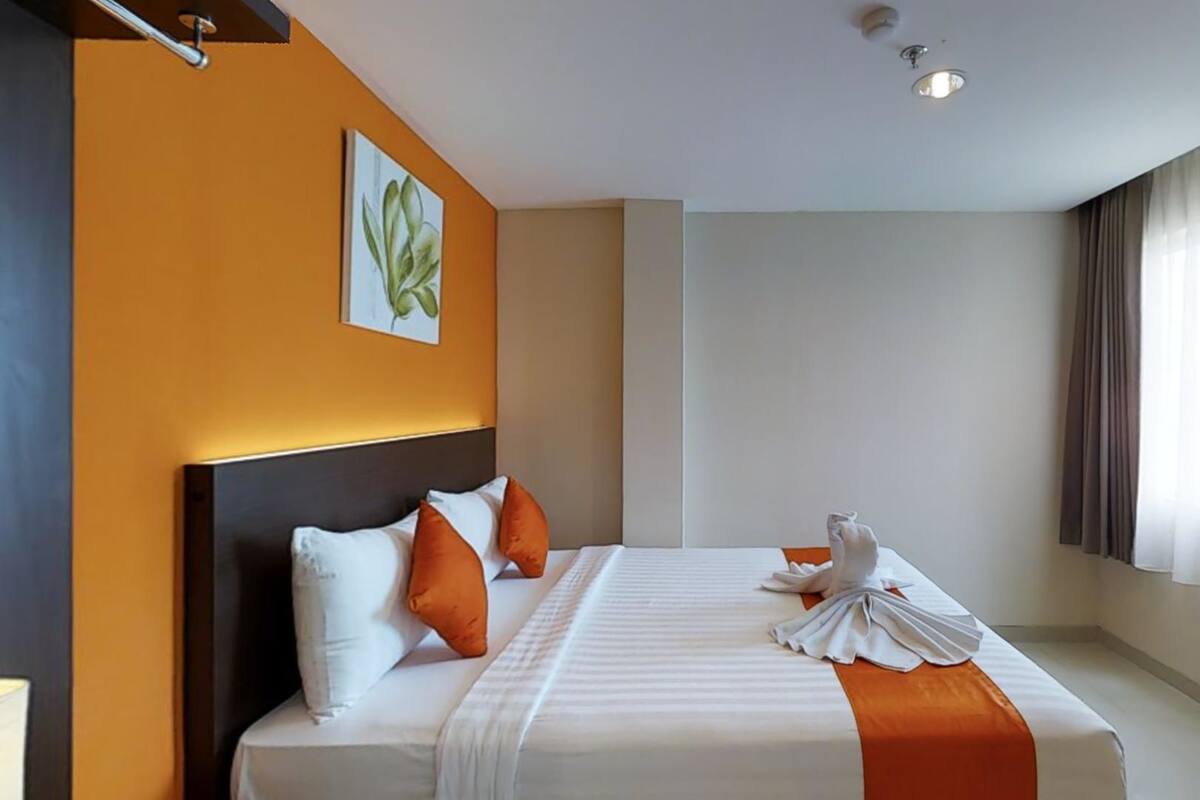 Quarto de hotel com uma cama grande, cabeceira, um quadro na parede e uma janela com cortinas.