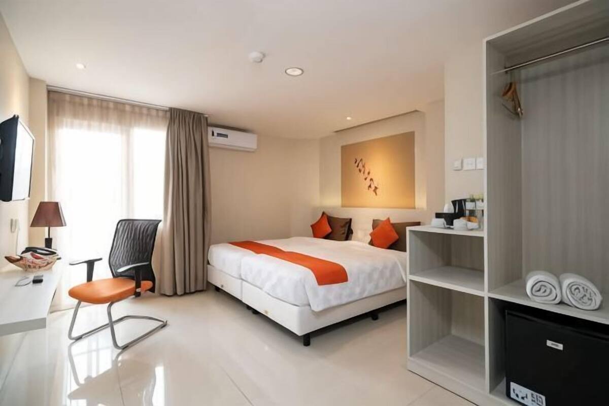 Quarto de hotel com cama, escrivaninha, cadeira, guarda-roupa e televisão.