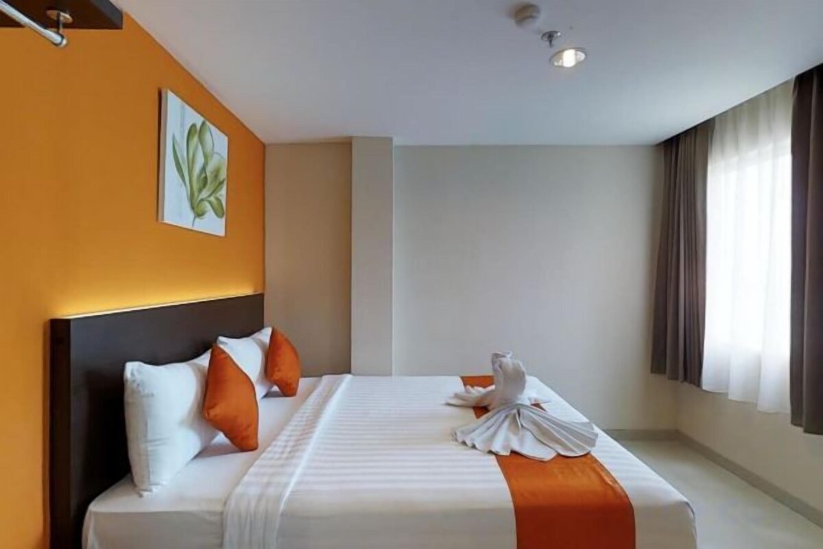 A hotel room with a bed, a headboard, a painting, and a window with curtains.