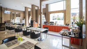 A spacious dining area with multiple tables and chairs, a buffet setup, and a large window providing natural light. - The Gloria Suites Jakarta (Jakarta)