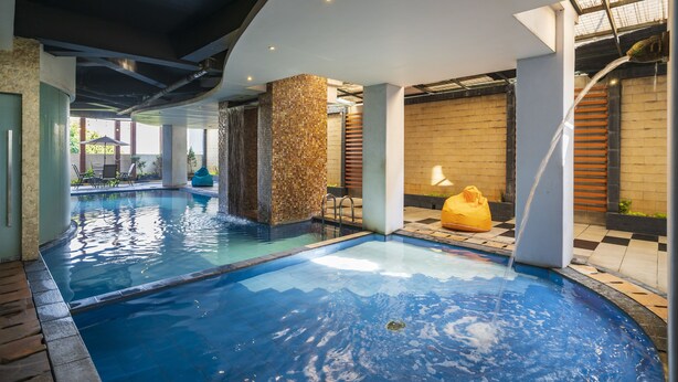 A swimming pool with a waterfall feature, surrounded by stone pillars and a checkered floor. - The Gloria Suites Jakarta (Jakarta)