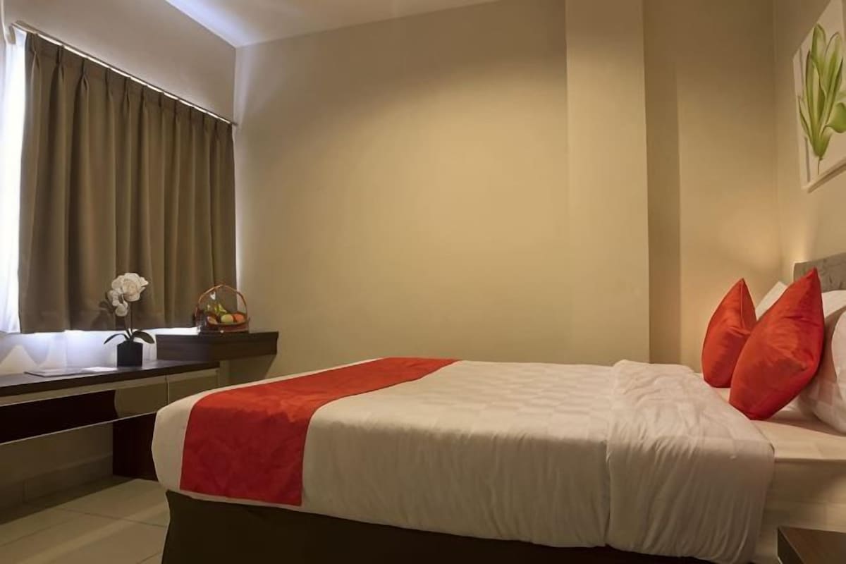 Una camera d'albergo con un letto, una finestra con tende, un comodino con un vaso e un'opera d'arte appesa al muro.
