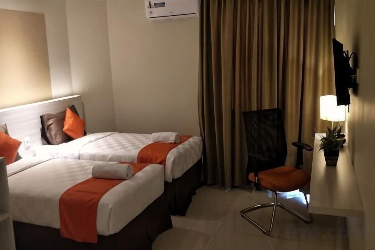A hotel room with two beds, a desk, a chair, an air conditioner, and a lamp.
