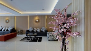 A modern living room with a sofa set, a coffee table, and decorative elements like a large artificial tree and wall sconces. - The Gloria Suites Jakarta (Jakarta)