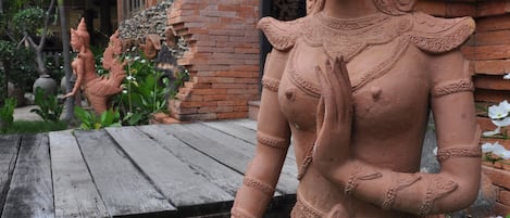 Una estatua de terracota de una deidad en un jardín, con un edificio de ladrillo al fondo.