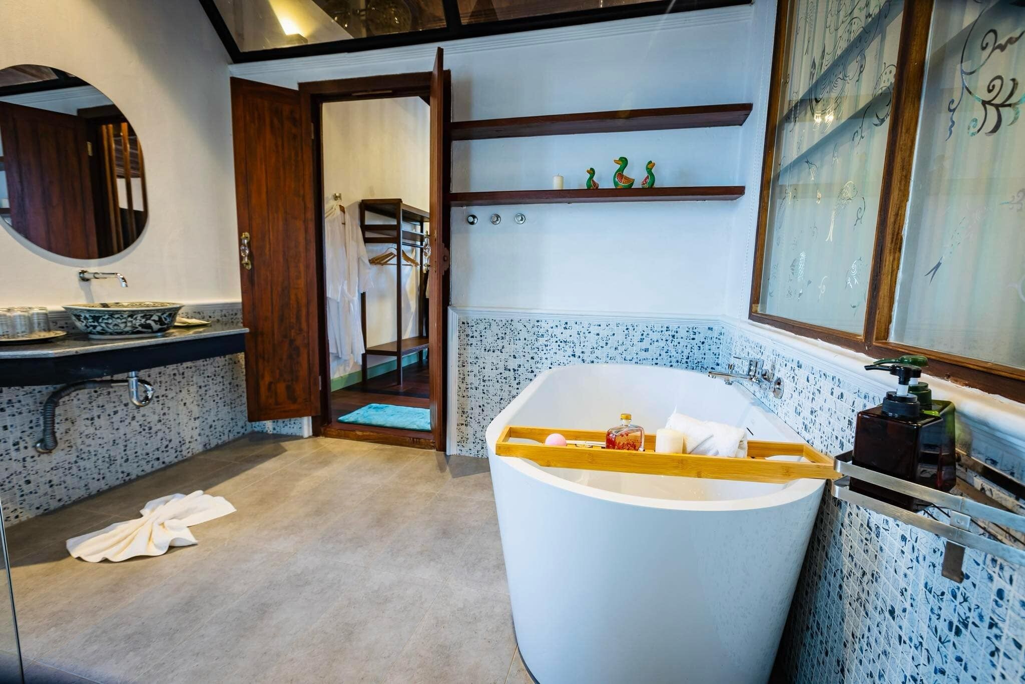 Une salle de bain moderne avec une baignoire sur pieds, un miroir rond et une étagère en bois agrémentée d’objets décoratifs.