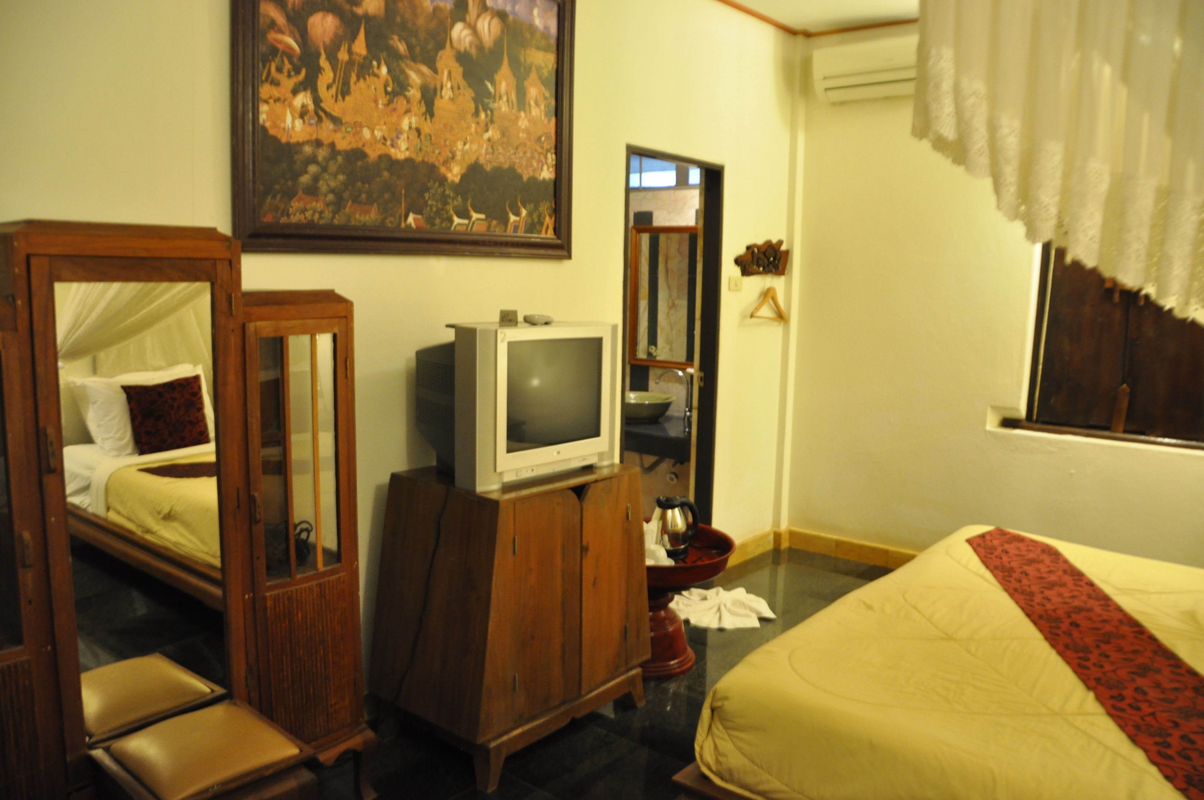 A hotel room with a bed, a wooden cabinet, a television, and a painting on the wall.