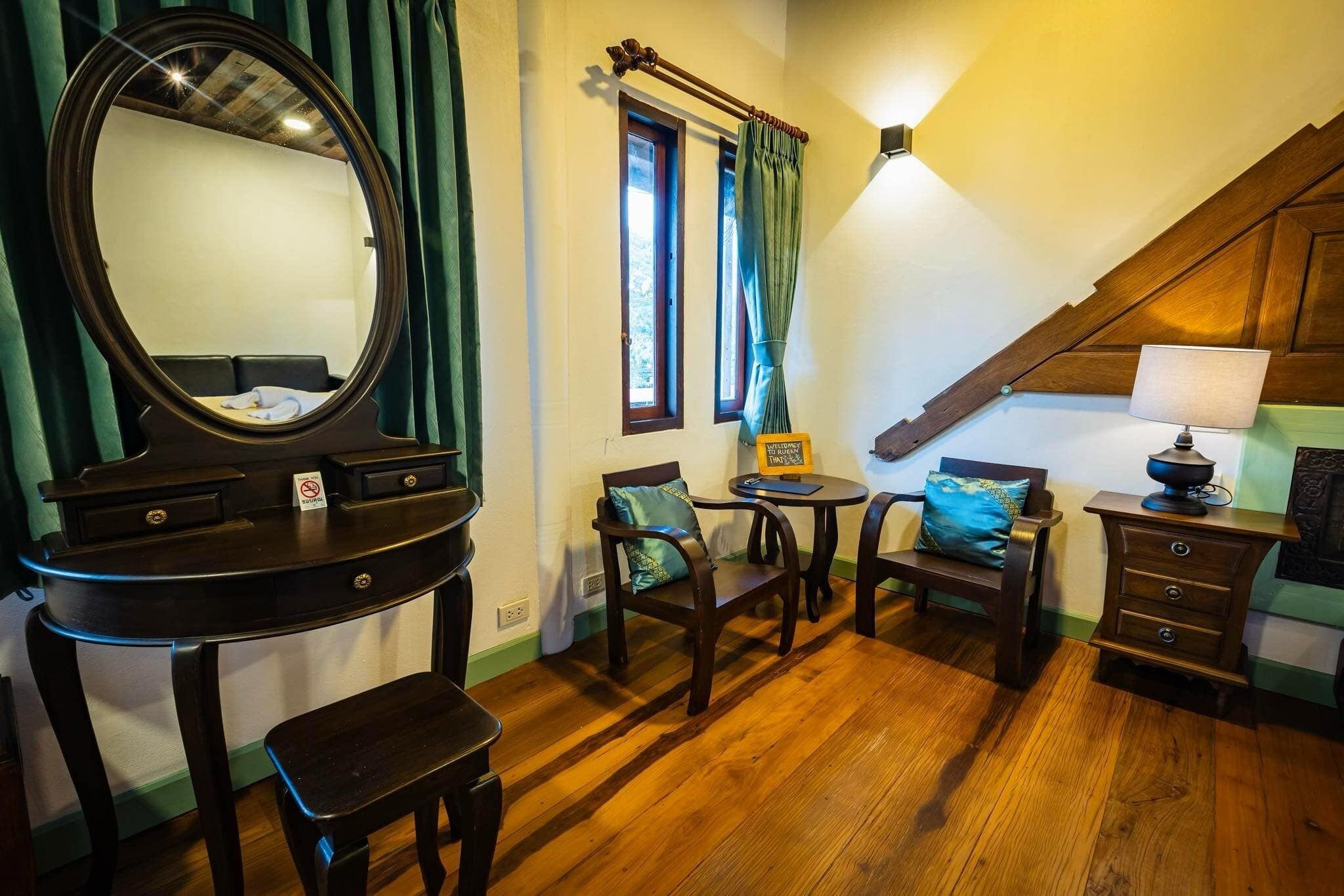 A room with a piano, a mirror, a small table with a lamp, and two chairs.