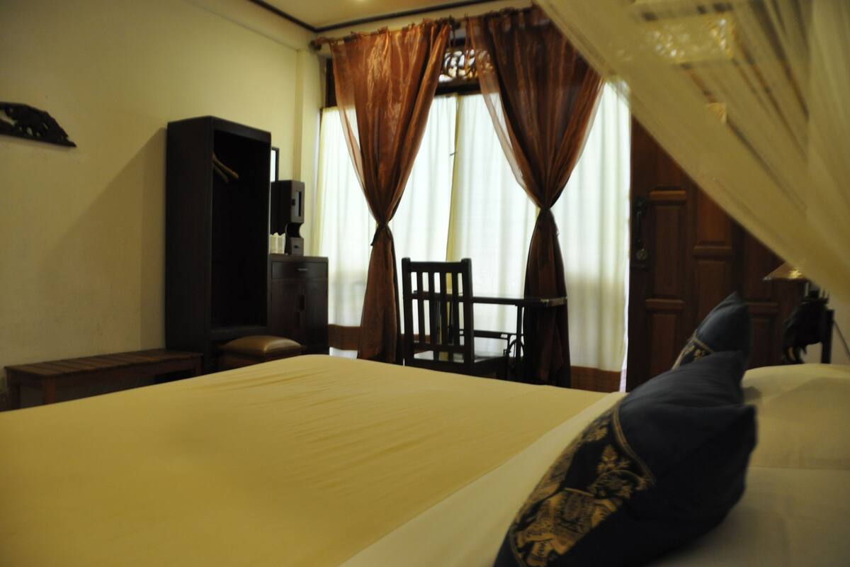 A hotel room with a bed, a wooden chair, a desk, and a wardrobe.