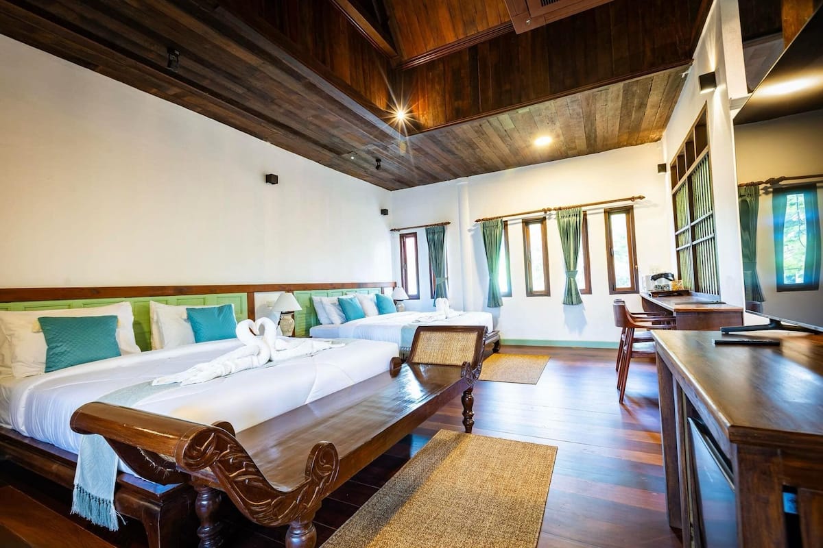 A hotel room with two beds, wooden furniture, a dining area, and large windows with curtains.