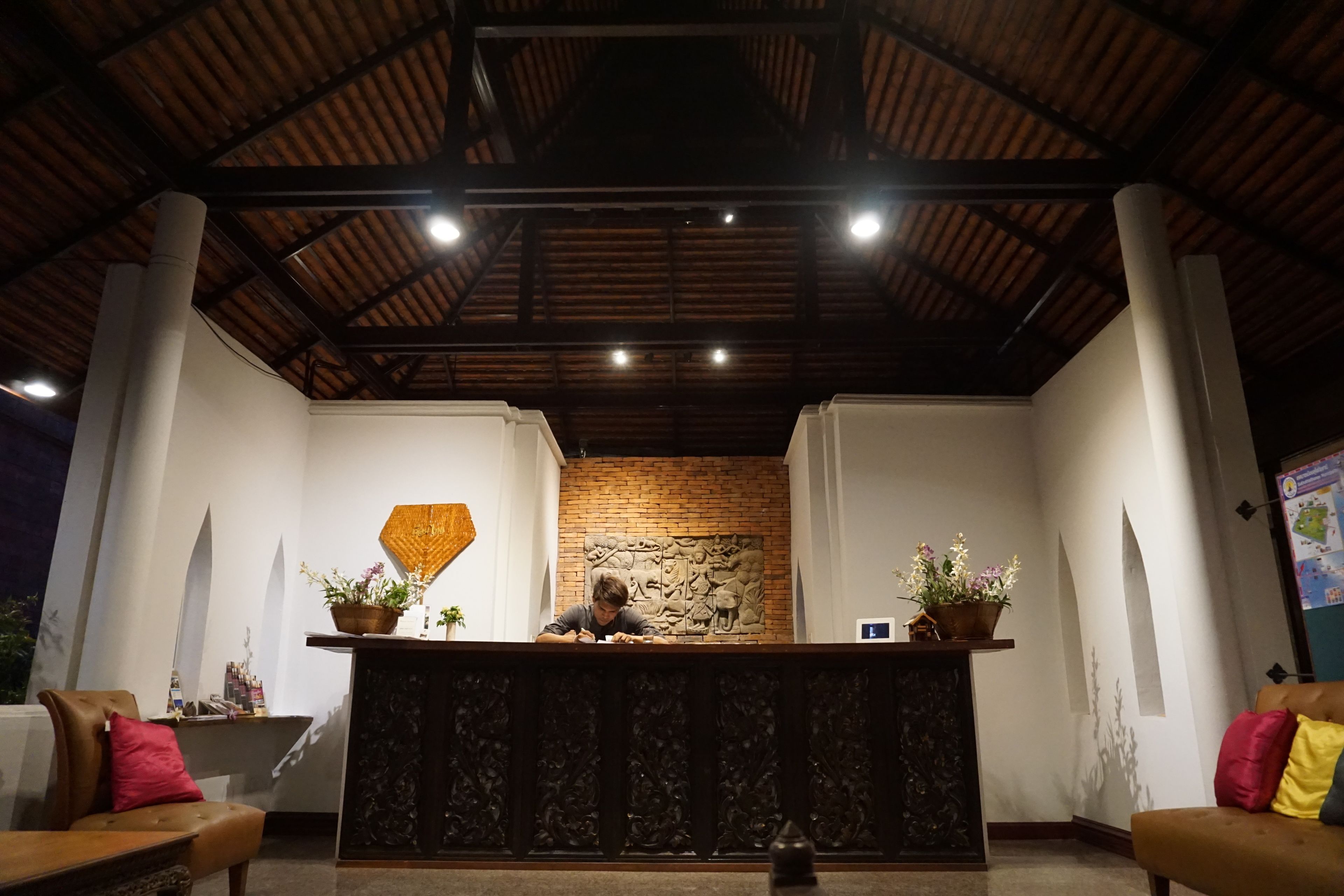 Un espace d’accueil doté d’un plafond en bois, d’un mur en briques orné d’une sculpture en relief et de deux plantes en pot posées sur un comptoir.
