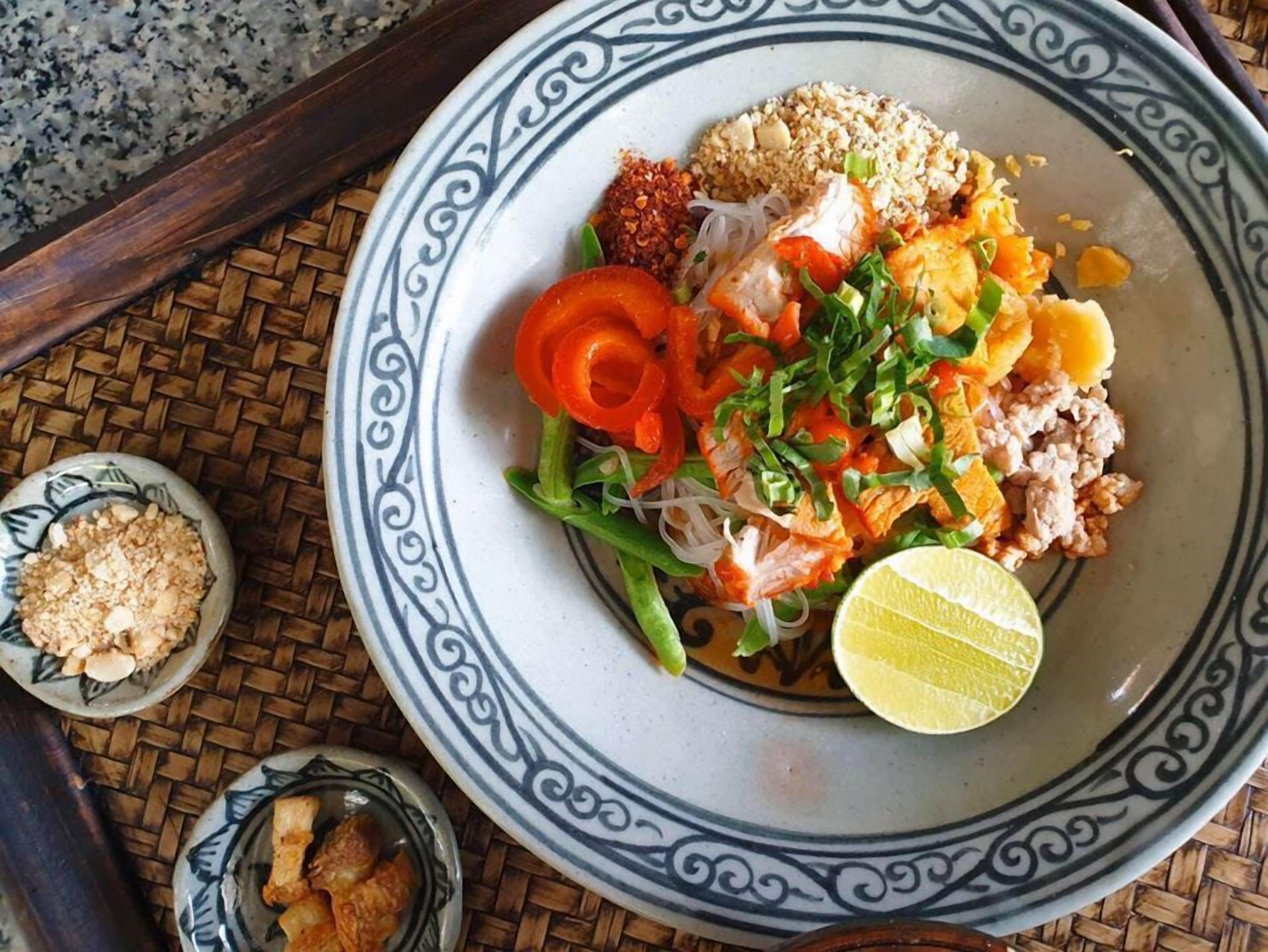 Un plato de comida con diversos ingredientes, como fideos, verduras y carne, sobre un plato decorativo.