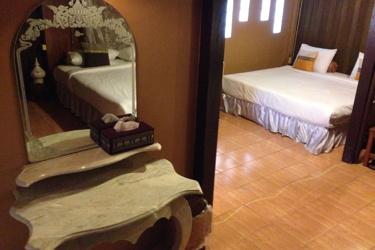 A hotel room with a bed, a bedside table with a tissue box, a mirror, and a wooden floor.