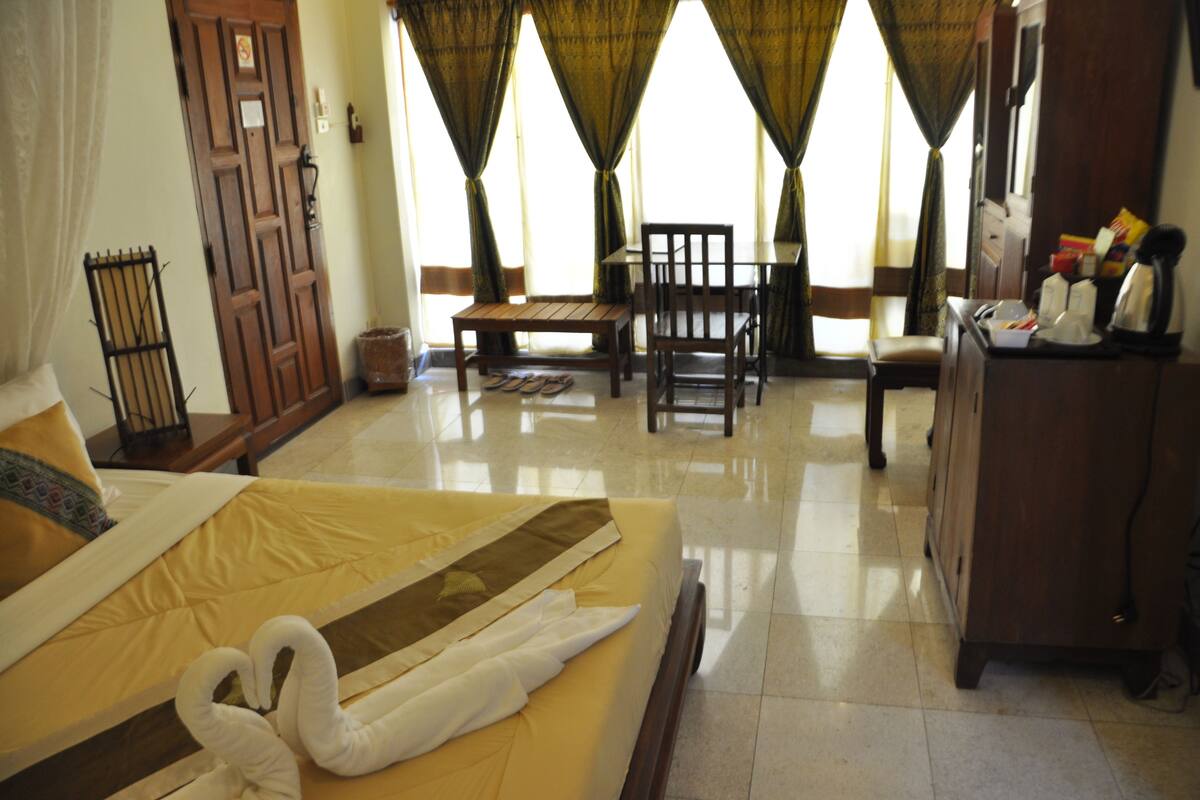 A hotel room with a bed, a wooden table, chairs, a desk, and a wardrobe.