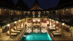 A pool area with lounge chairs and a dining area, surrounded by wooden buildings with a traditional architectural style. - Ruean Thai Hotel (Sukhothai)