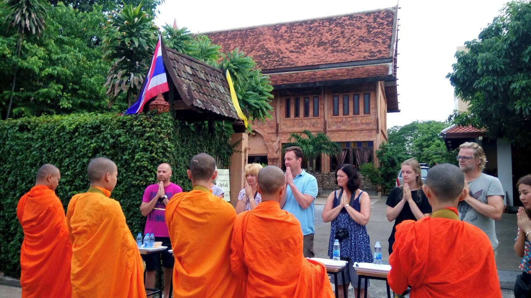 A group of people in orange robes standing in front of a building with a tiled roof.