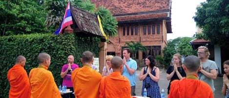 A group of people in orange robes standing in front of a building with a tiled roof.