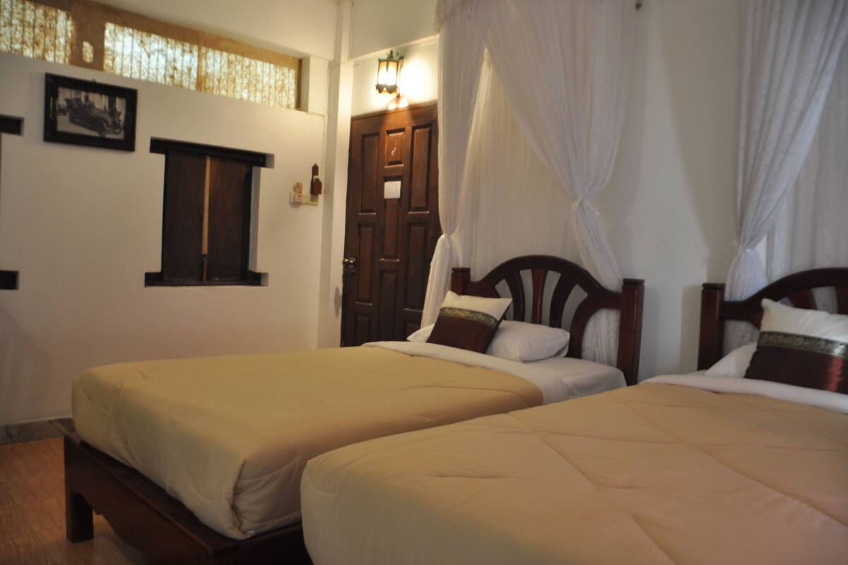 A room with two beds, a wooden door, and a window with a picture frame.
