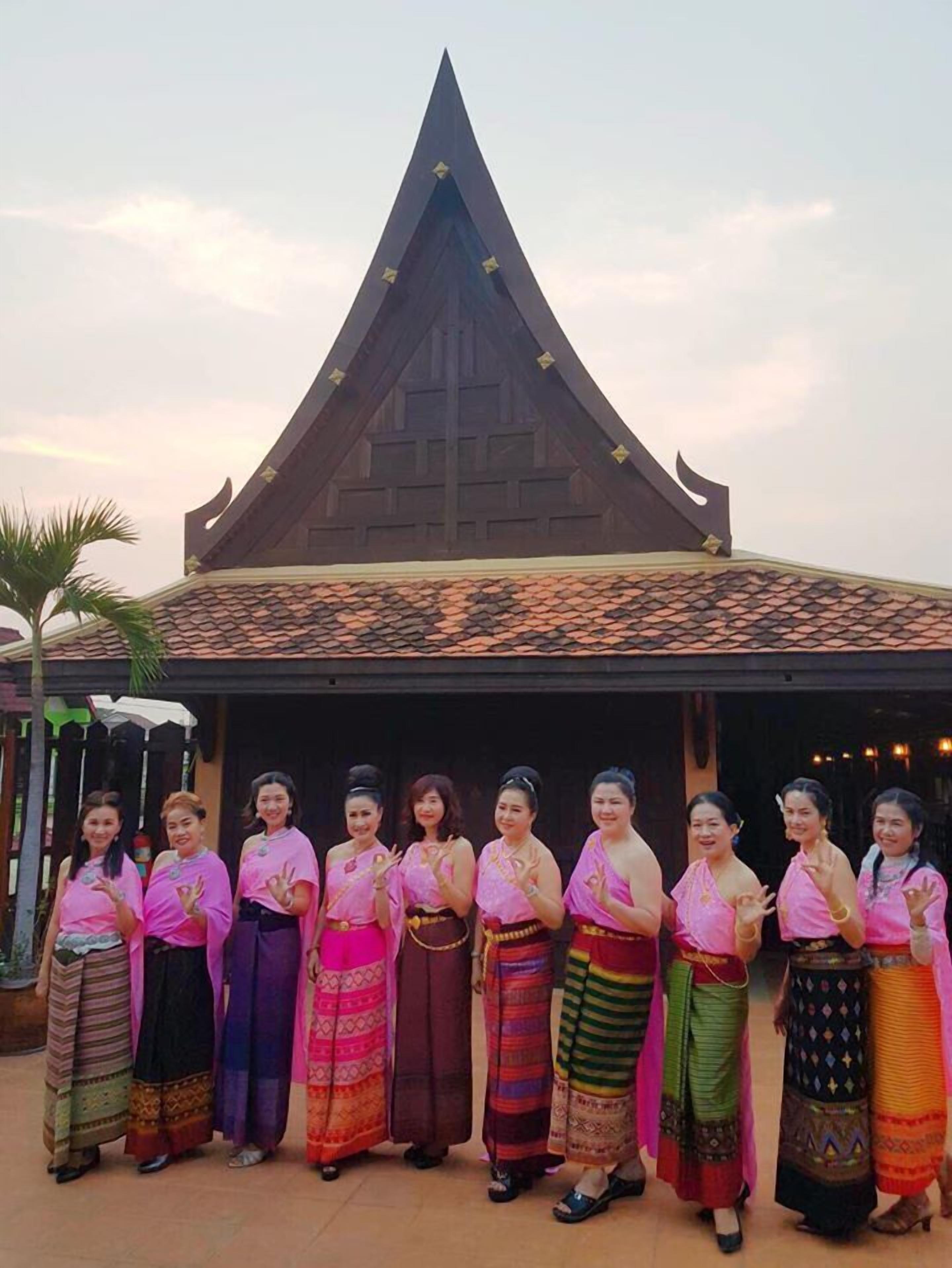 A group of women in traditional attire standing in front of a building with a pointed roof.