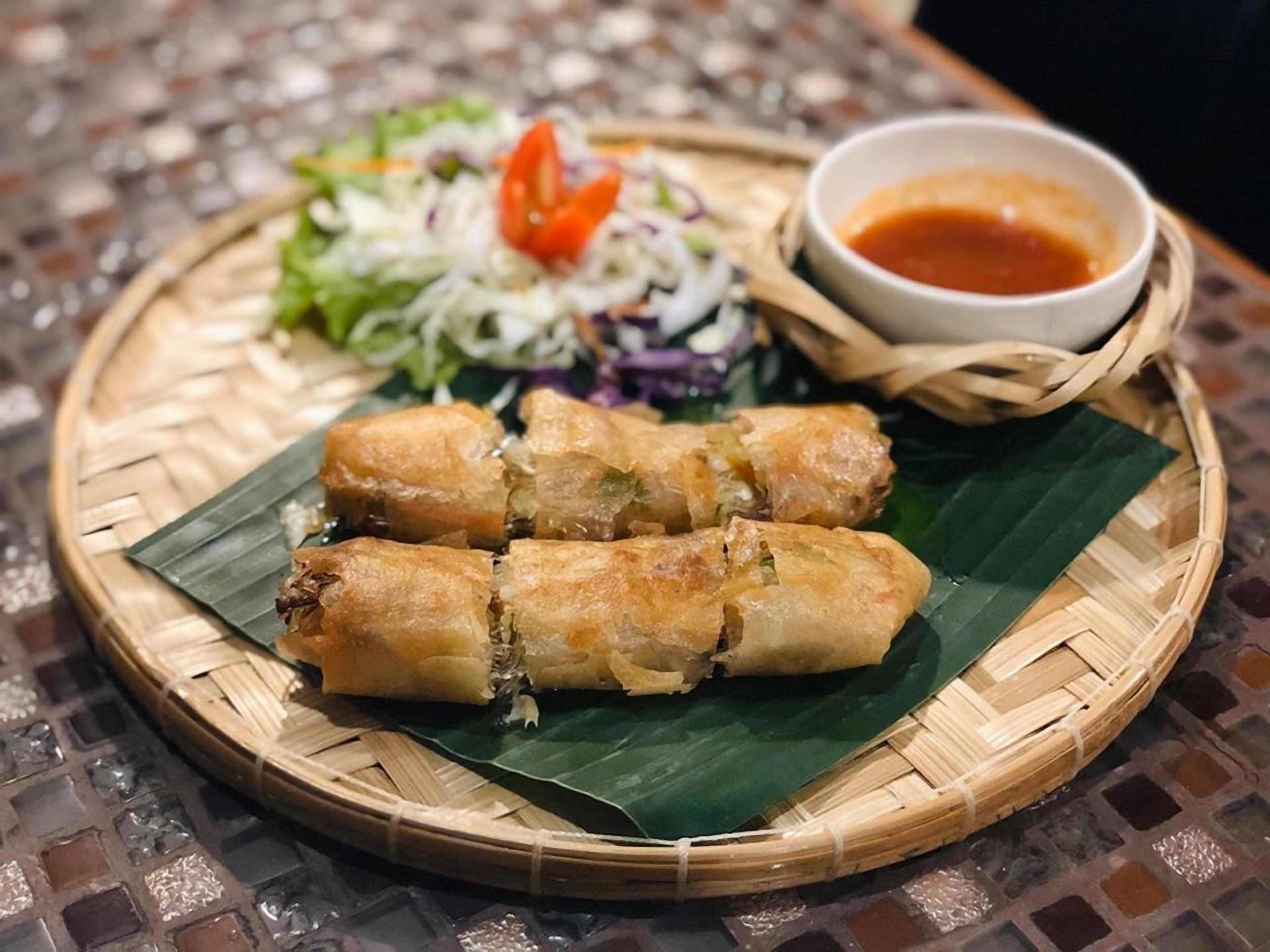 A plate of spring rolls with a side salad and dipping sauce.