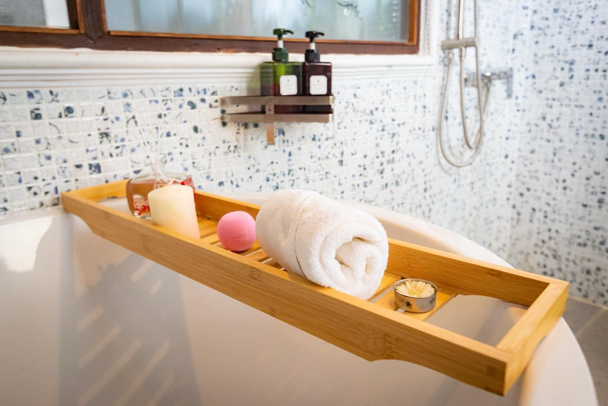 A bathroom with a wooden tray holding a towel, a pink bath ball, and a candle. There are two soap dispensers on a shelf above the tray.