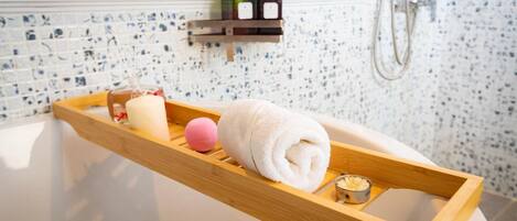 A bathroom with a wooden tray holding a towel, a pink bath ball, and a candle. There are two soap dispensers on a shelf above the tray.